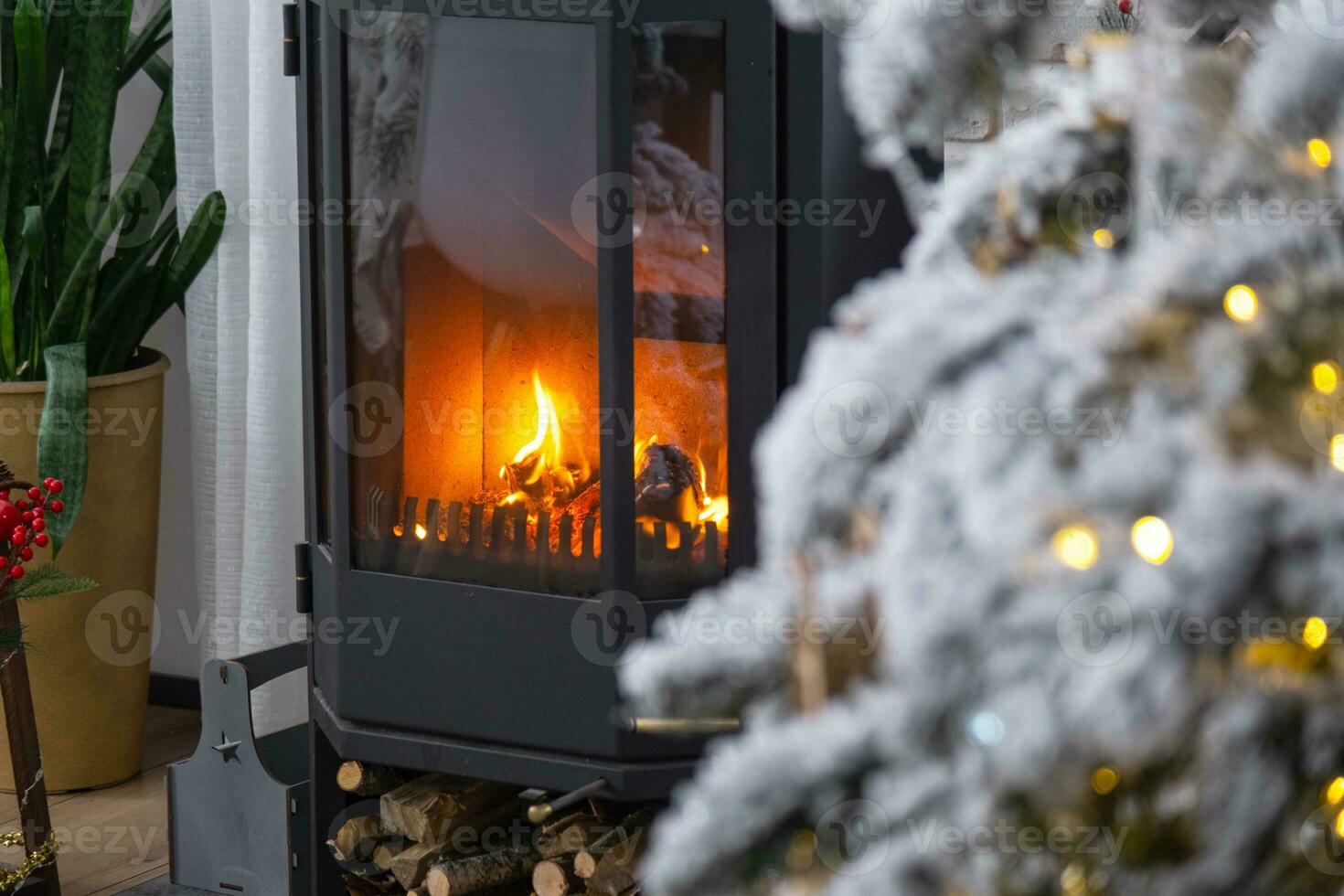 Metall black stove, burning hearth fireplace in white Festive interior of house is decorated for Christmas and New Year, Christmas tree. firewood in the woodpile, cozy and heating of home photo