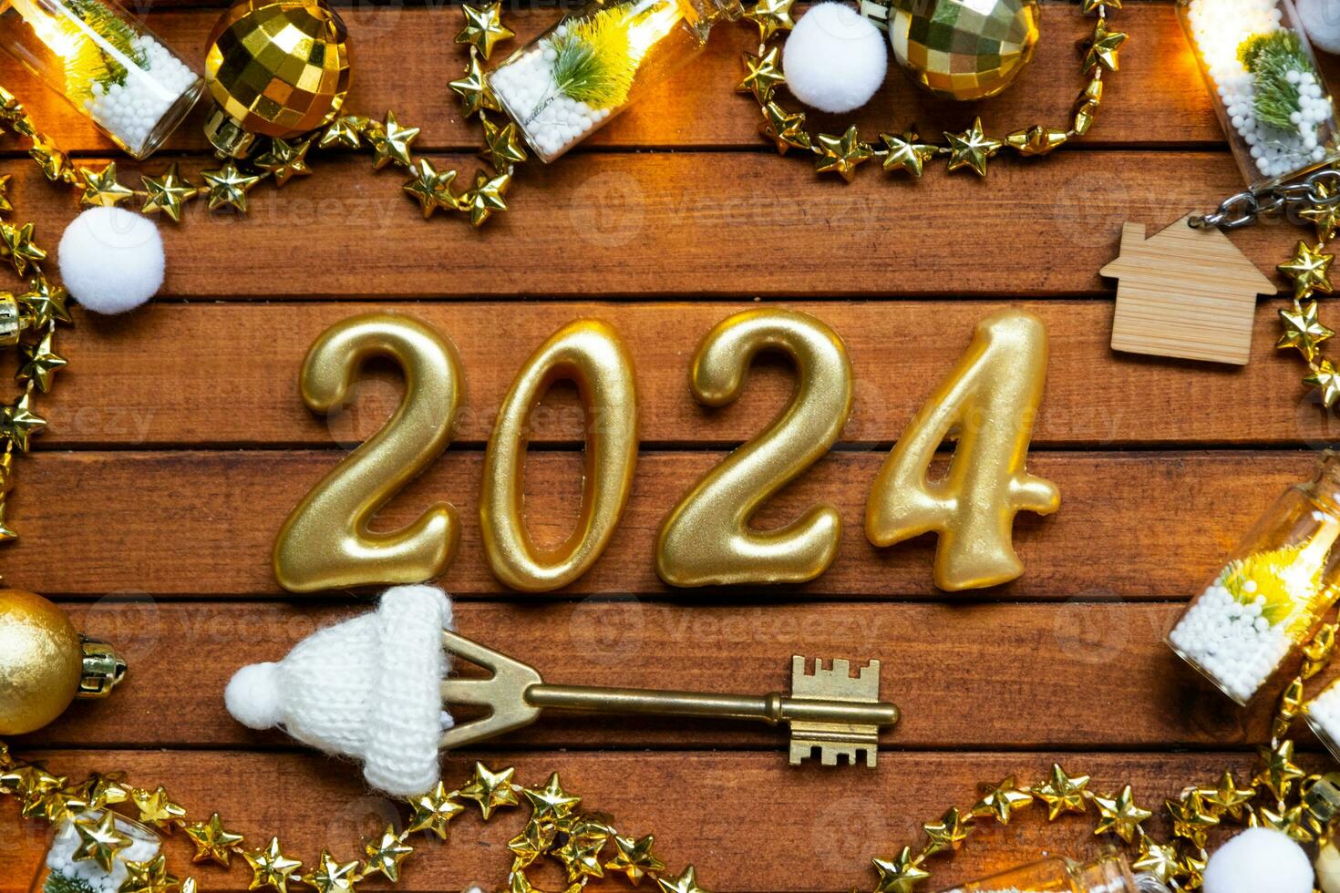 House key with keychain cottage on festive brown wooden background with stars, lights of garlands. New Year 2024 wooden letters, greeting card. Purchase, construction, relocation, mortgage, insurance photo