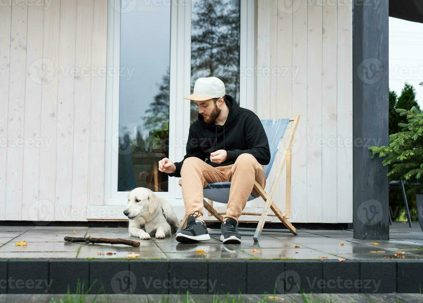 un joven hombre descansa cerca su país casa con un perro. foto