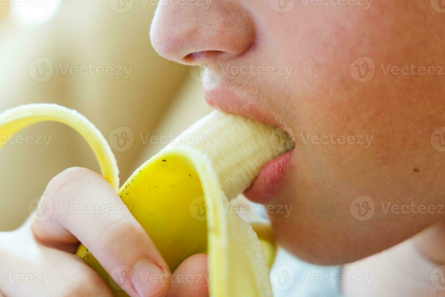 Portrait of a teenage boy eating a banana. Photo of a guy's mouth and lips with a banana. Fresh fruit. Healthy foods for children