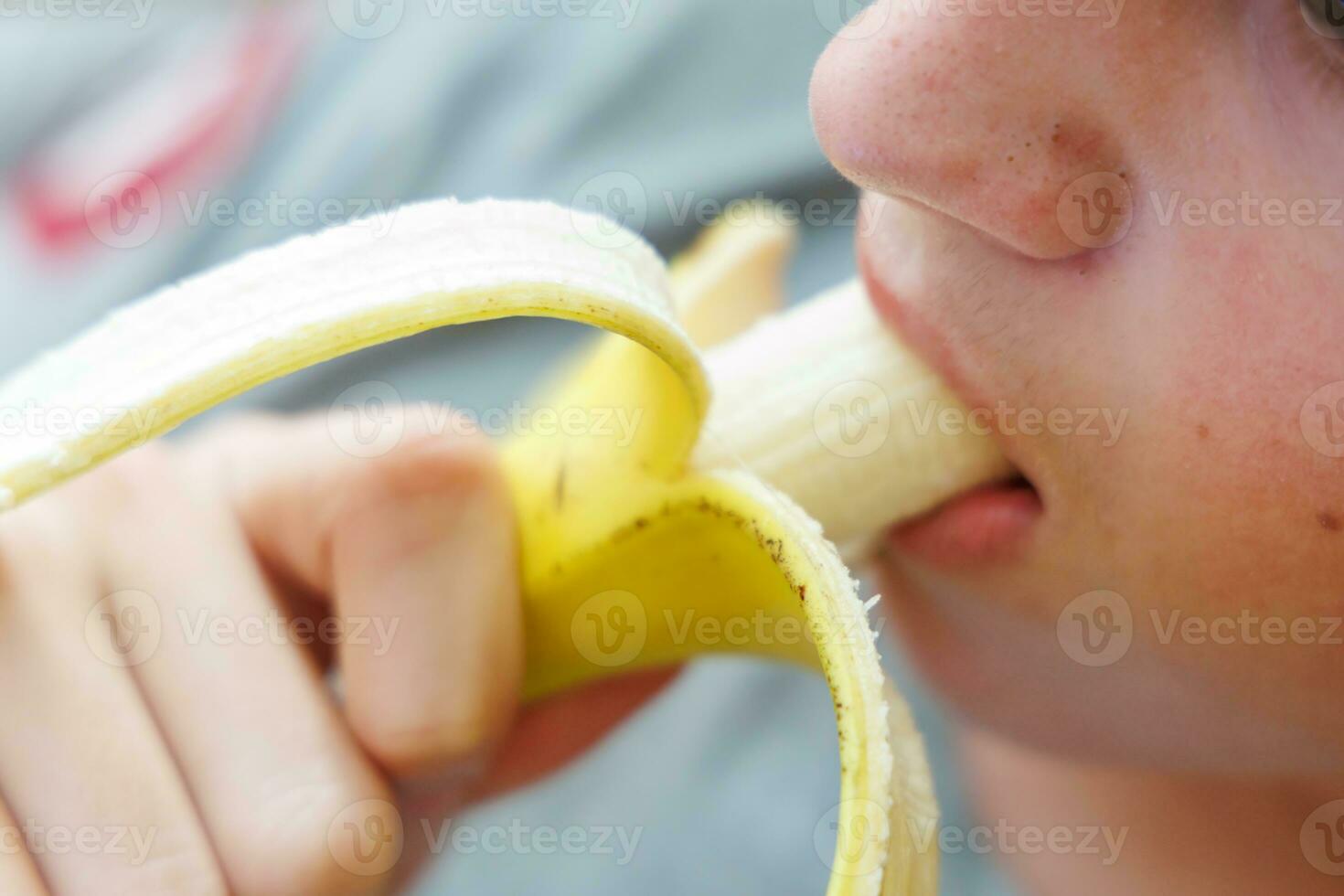 Portrait of a teenage boy eating a banana. Photo of a guy's mouth and lips with a banana. Fresh fruit. Healthy foods for children