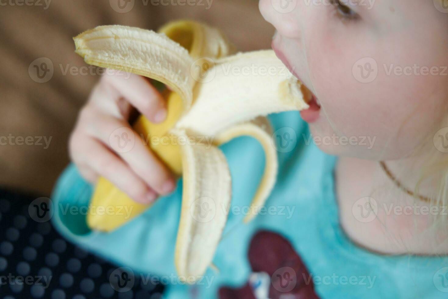 Portrait of a little girl eating a banana. The concept of healthy food. A fresh quick snack photo