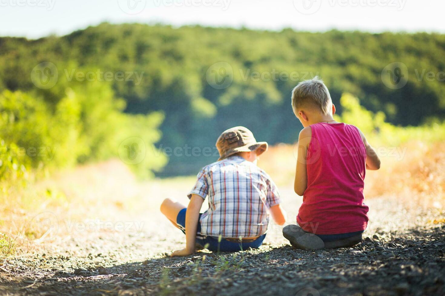 Two boys and a black dog sitting on the road in the forest photo