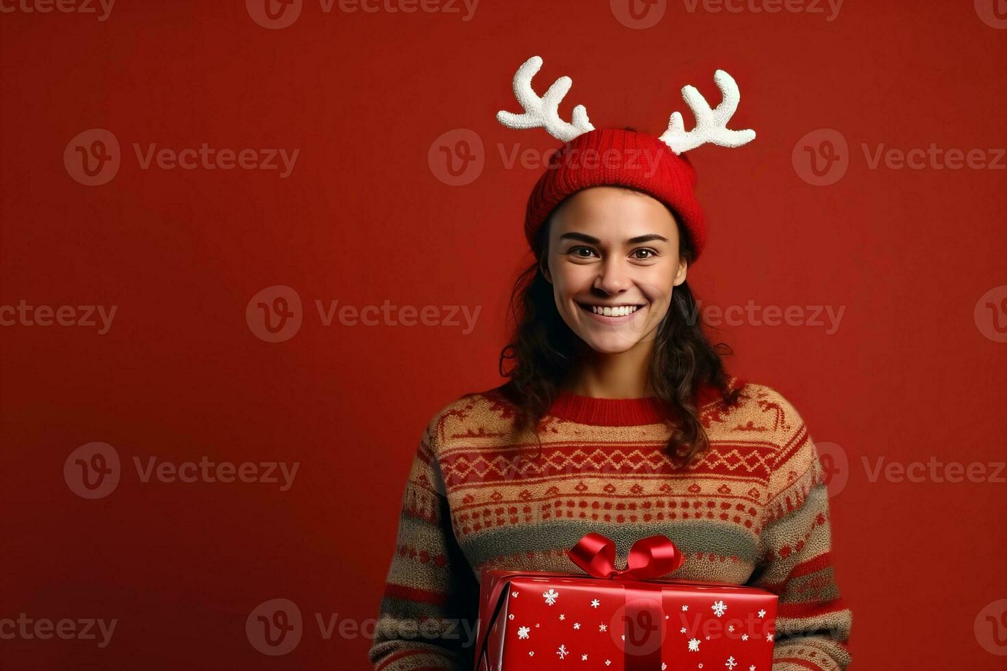 AI generated Portrait of a happy young woman in christmas sweater with reindeer horns holding present box isolated over red background photo