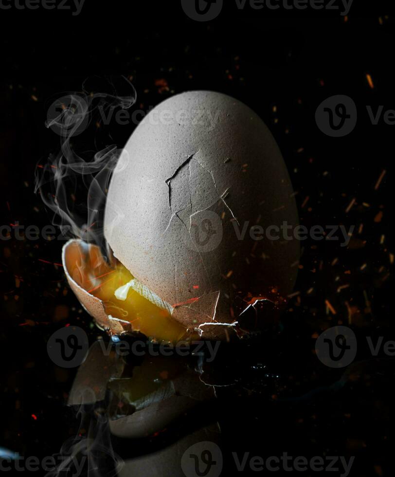 fresh broken egg with yolk sticking out on black background photo