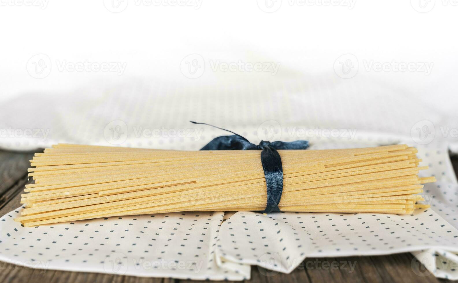 group of uncooked italian spaghetti pasta tied together by blue silk ribbon photo