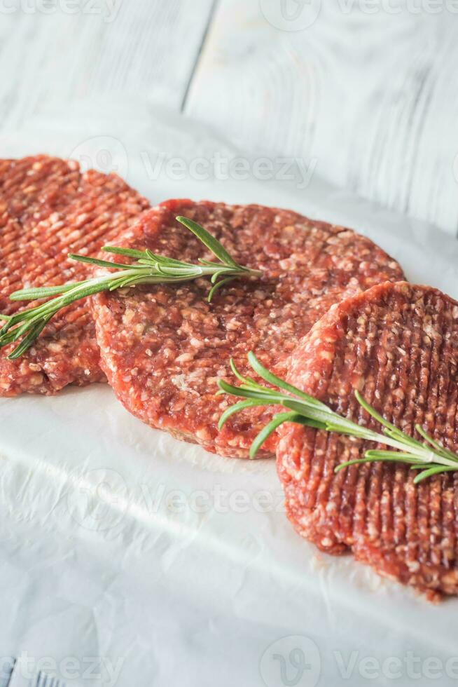 Raw beef patties on the white parchment photo