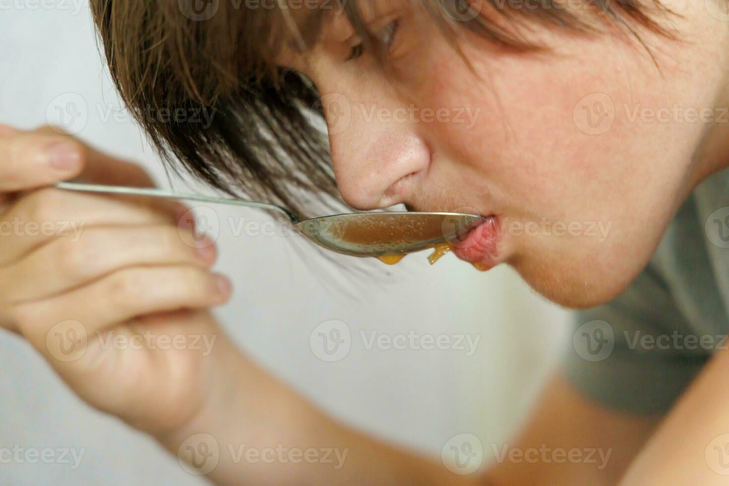 retrato de un adolescente comiendo sopa de remolacha con un cuchara. de cerca foto