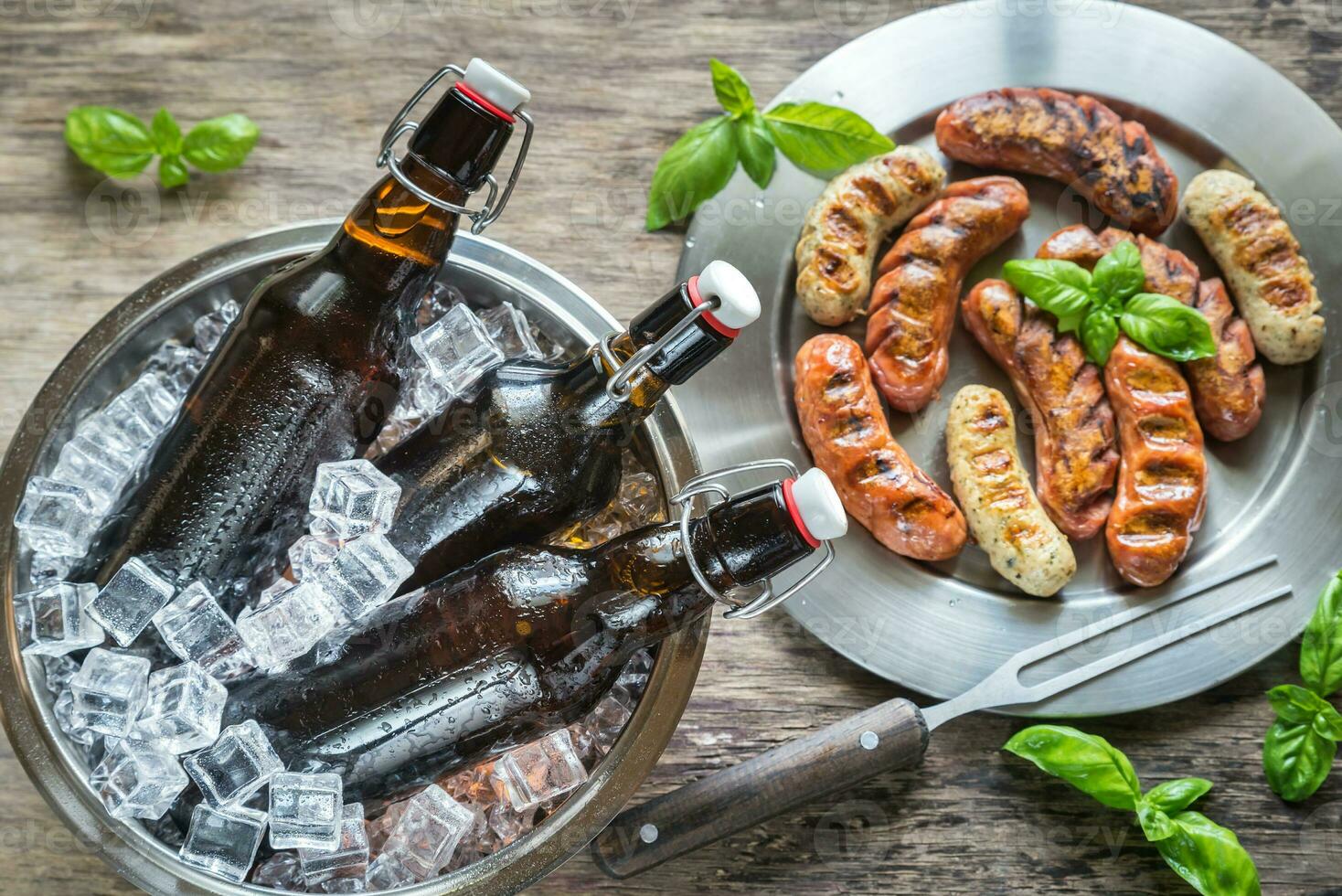 A la parrilla salchichas con botellas de cerveza foto