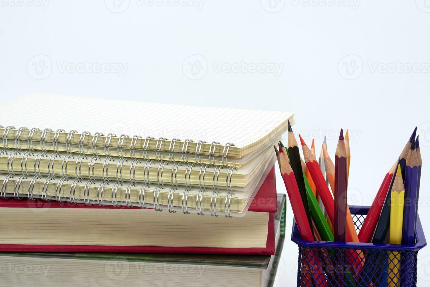 Crayon or colored pencils in box with side stack of books and school supplies on with background. Learning, study and office equipment concept. photo