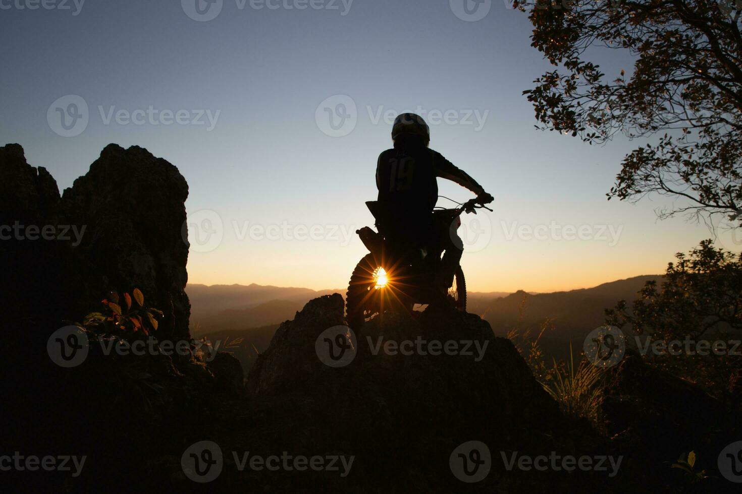 Man with motocross bike against beautiful lights, silhouette of a man with motocross motorcycle On top of rock high mountain at beautiful sunset, enduro motorcycle travel concept. photo