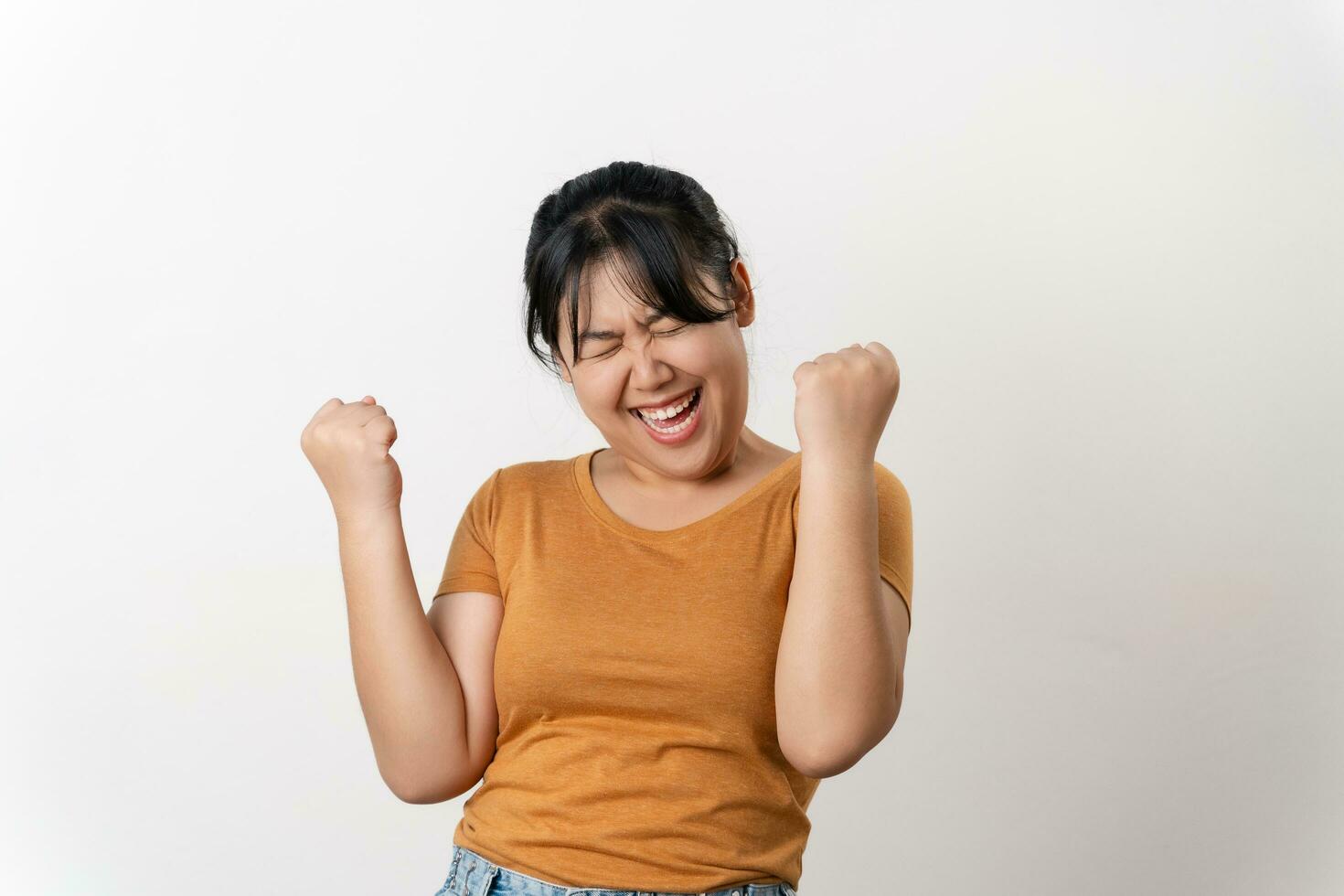 Happy successful young Asian woman expressing joy and excitement by raising her arms in a triumphant gesture standing on white background. photo