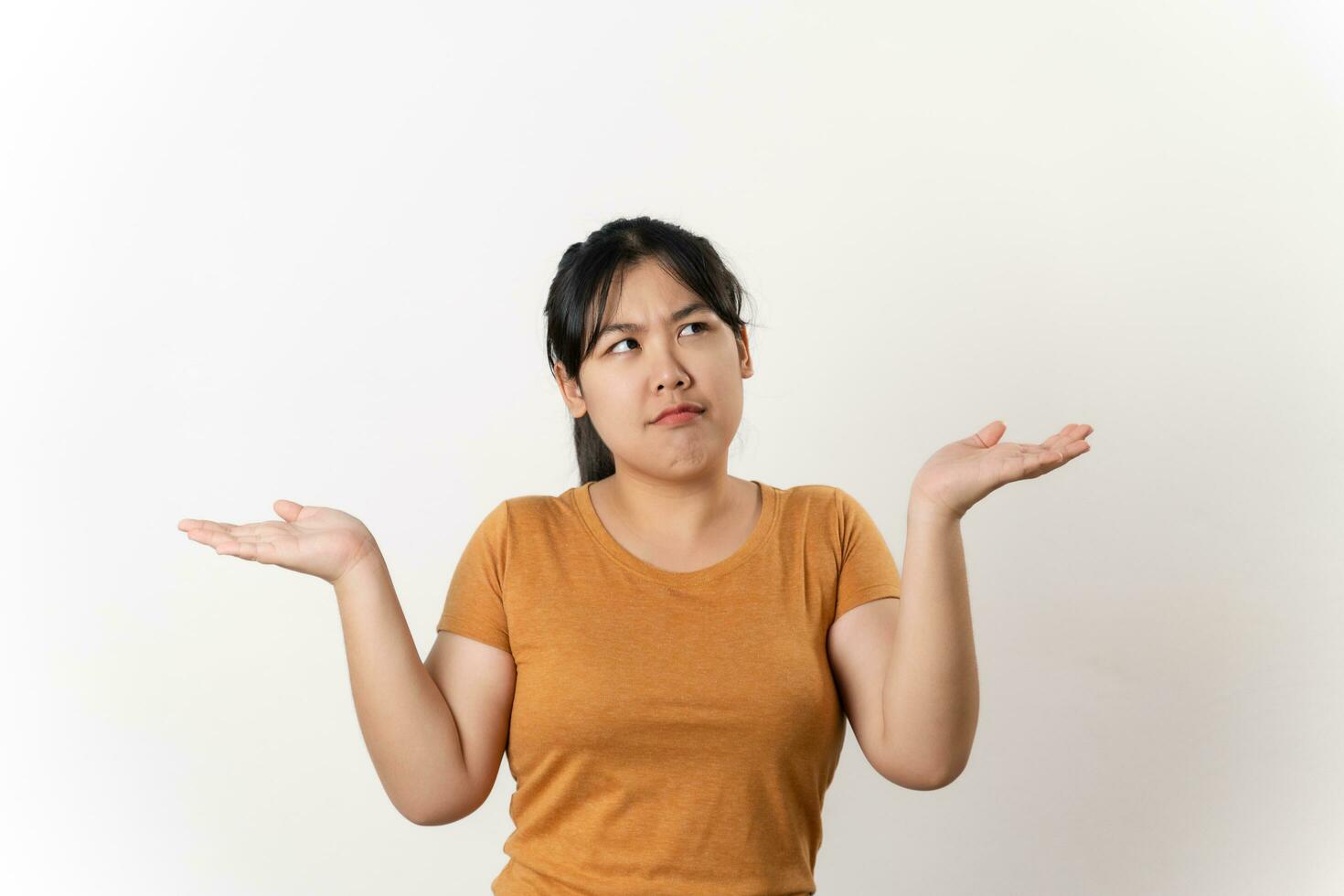 The confused beautiful Asian woman shrugging shoulders spreads hands sideways standing on white background. bewilderment, doubting, have no idea, don't know. photo