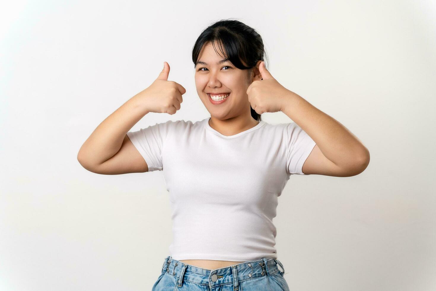 The portrait of beautiful young Asian woman showing thumb up hand sign on white background. Agreement, approval, recommending, like Concept. photo