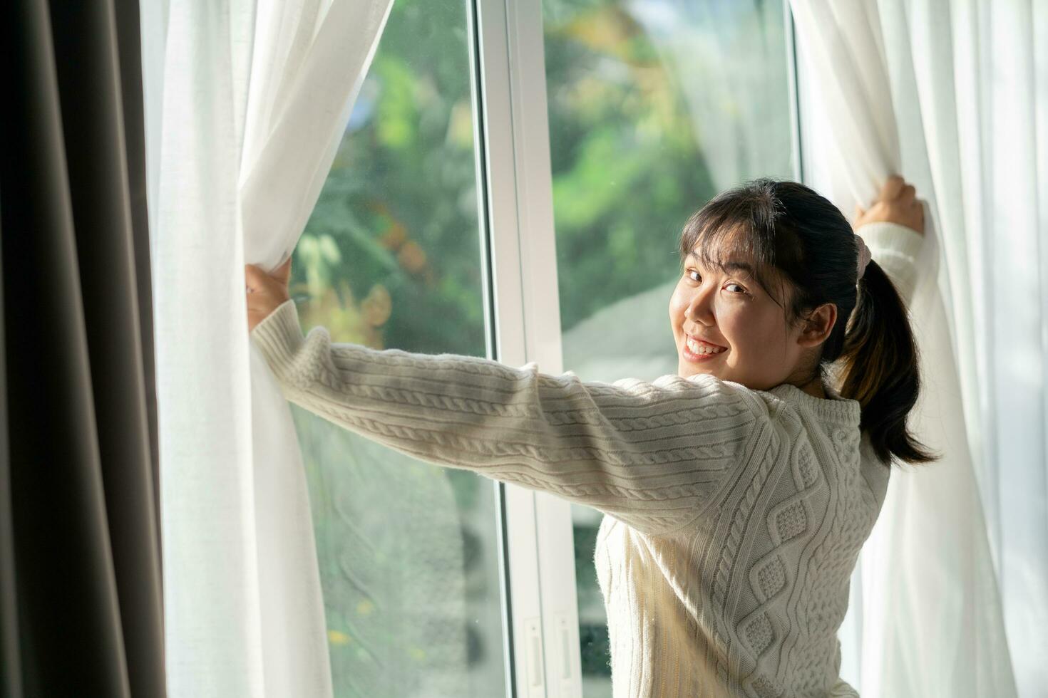 contento mujer apertura ventana cortinas en el Mañana a hogar. foto