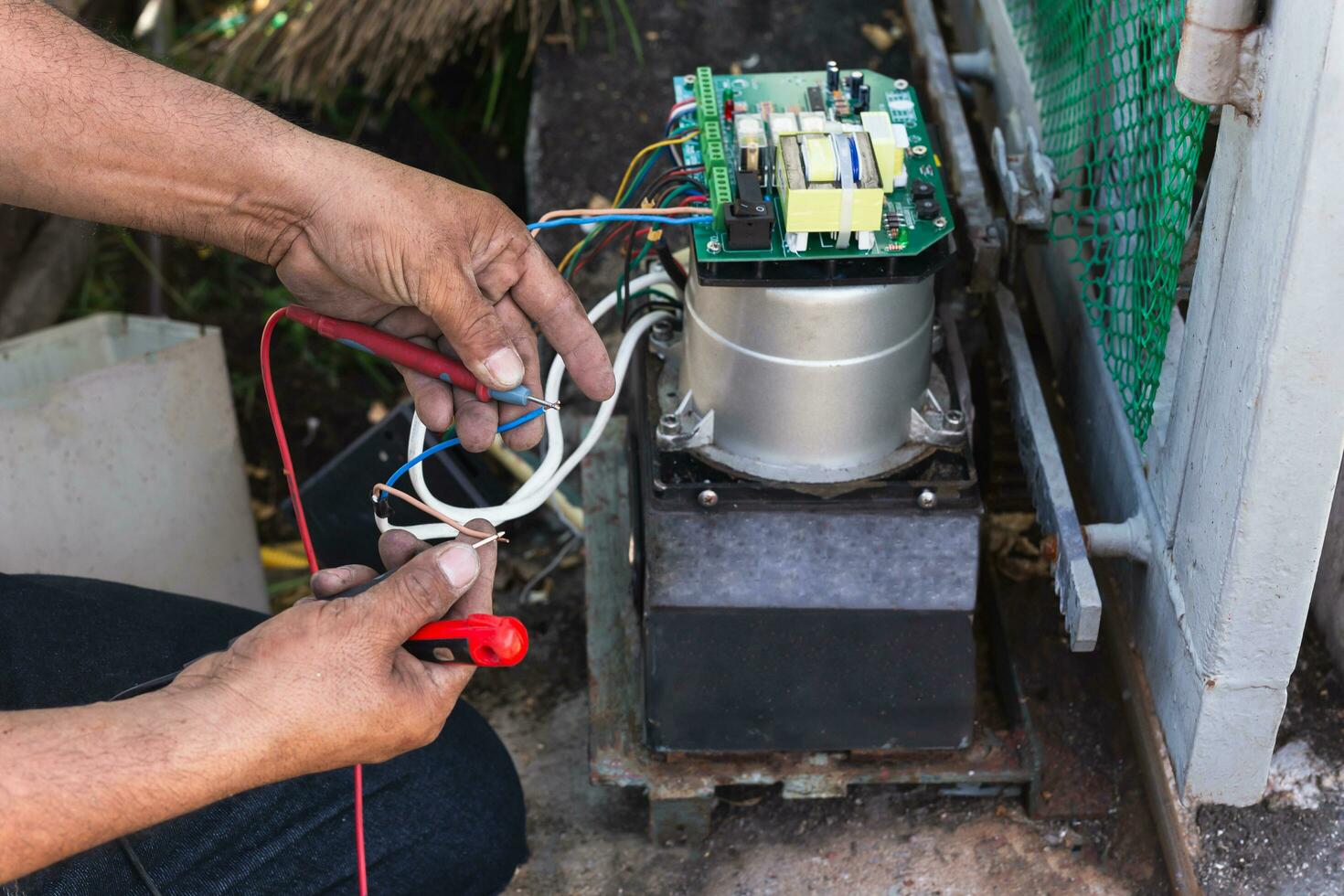 Hands of an electrician with multimeter probe at electric board panel. photo