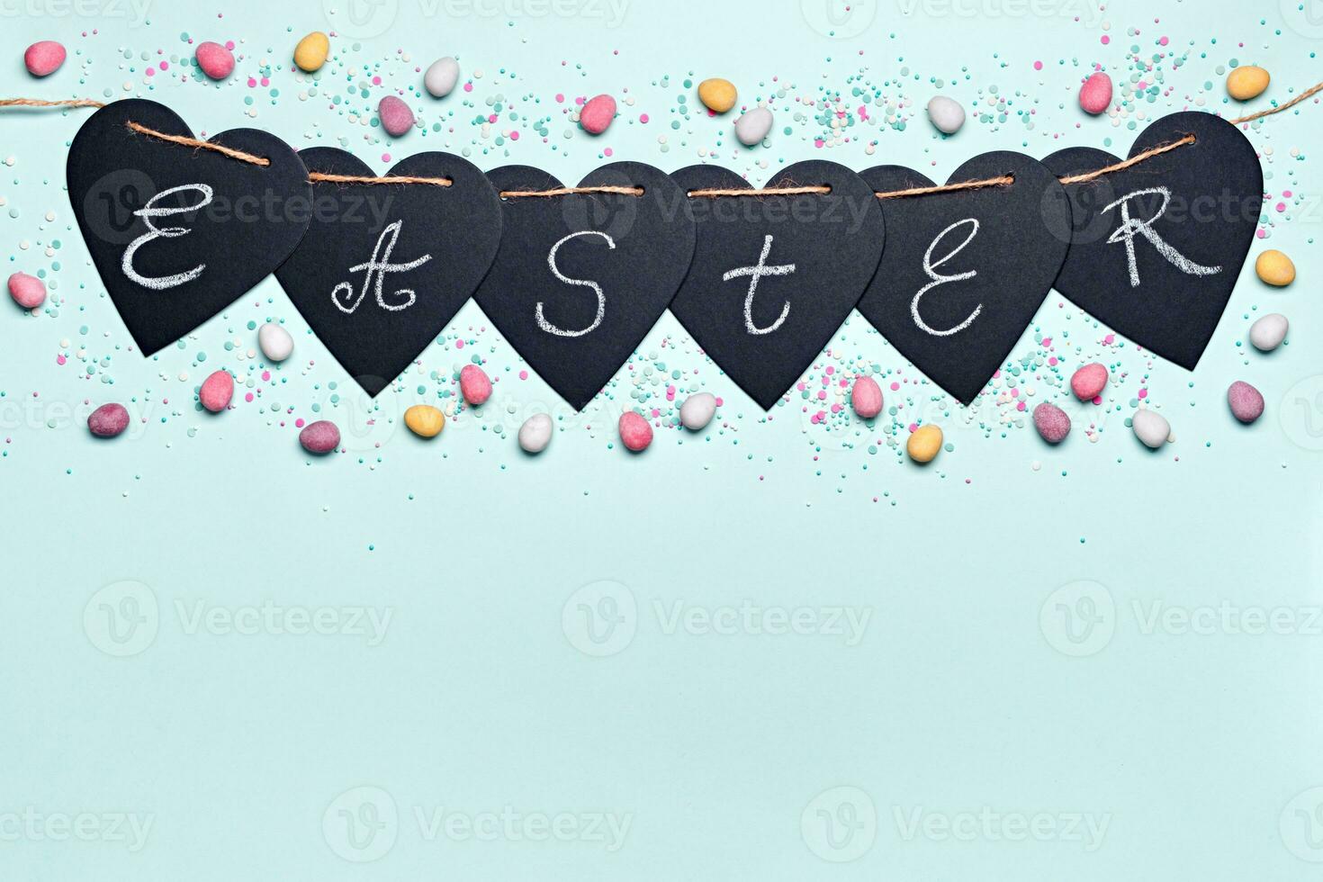Happy easter greeting card. Garland with Easter word and chocolate eggs in sugar glaze on blue background. Flat lay photo