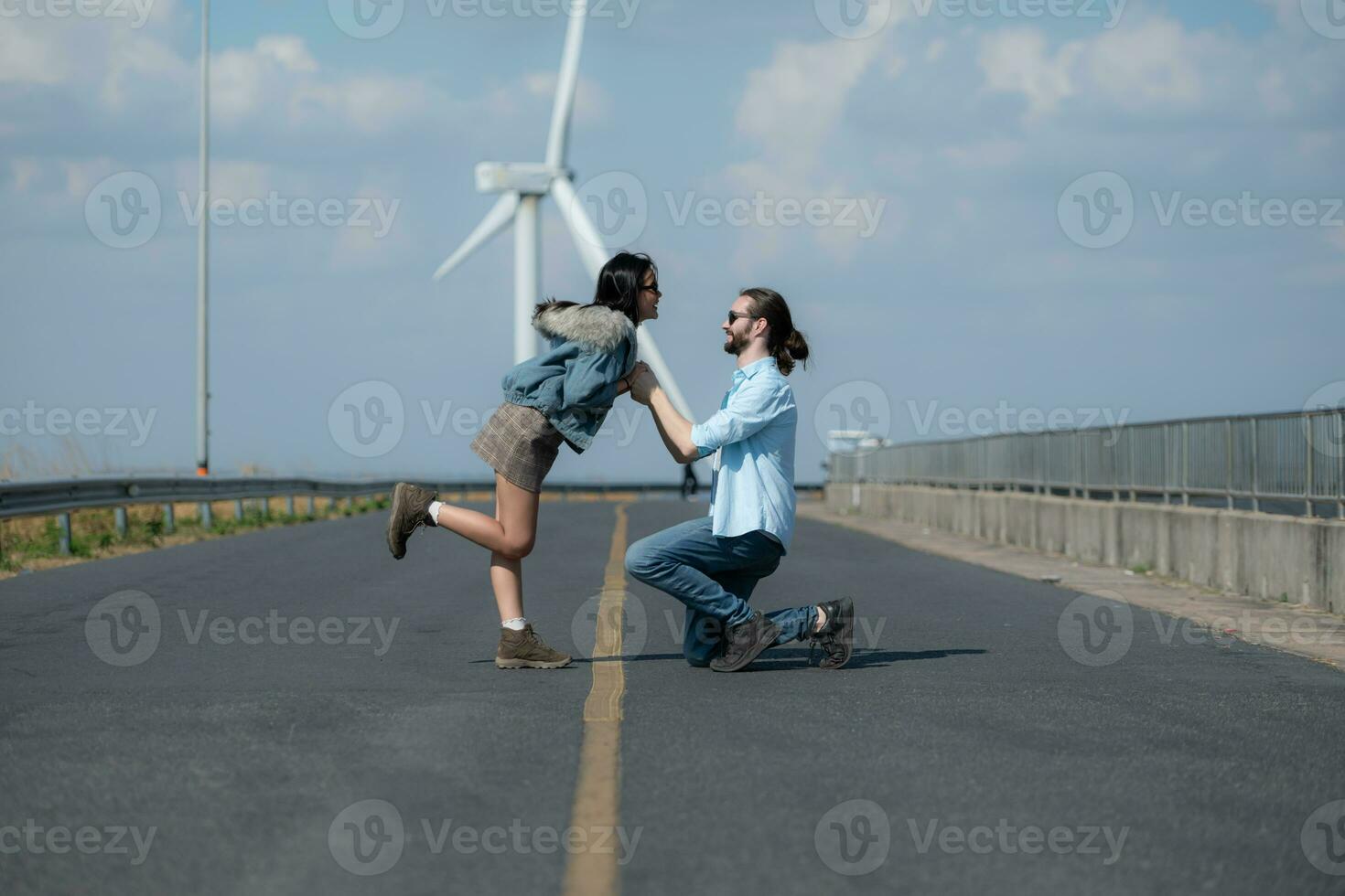 On the road, a young couple proposes to each other, with wind turbines in the background. photo