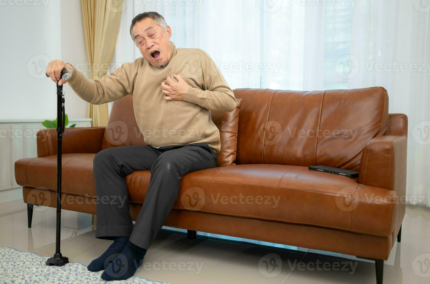 With heart disease symptoms, a senior guy sits on a sofa with a walking stick in his living room at home. photo