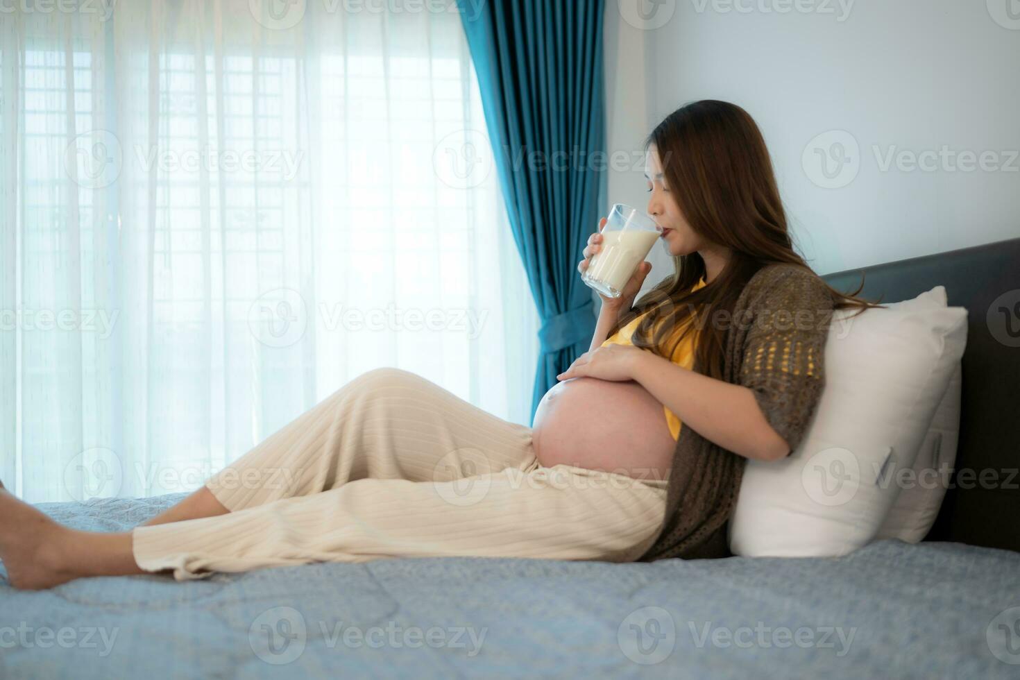 Portrait of beautiful asian pregnant woman drinking milk in bedroom at home photo