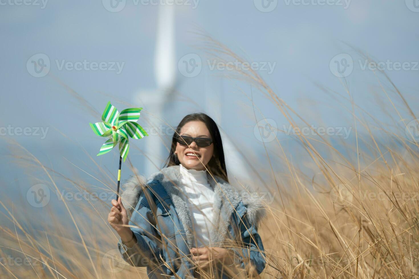 Young gorgeous brunette woman with long hair wearing a blue jacket, black sunglasses, and holding a miniature windmill photo