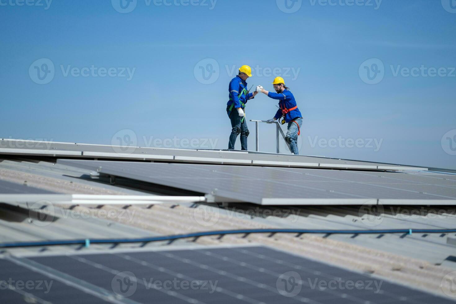 A young technician intern working on solar panels is fear of heights with senior engineers who are always helping out photo