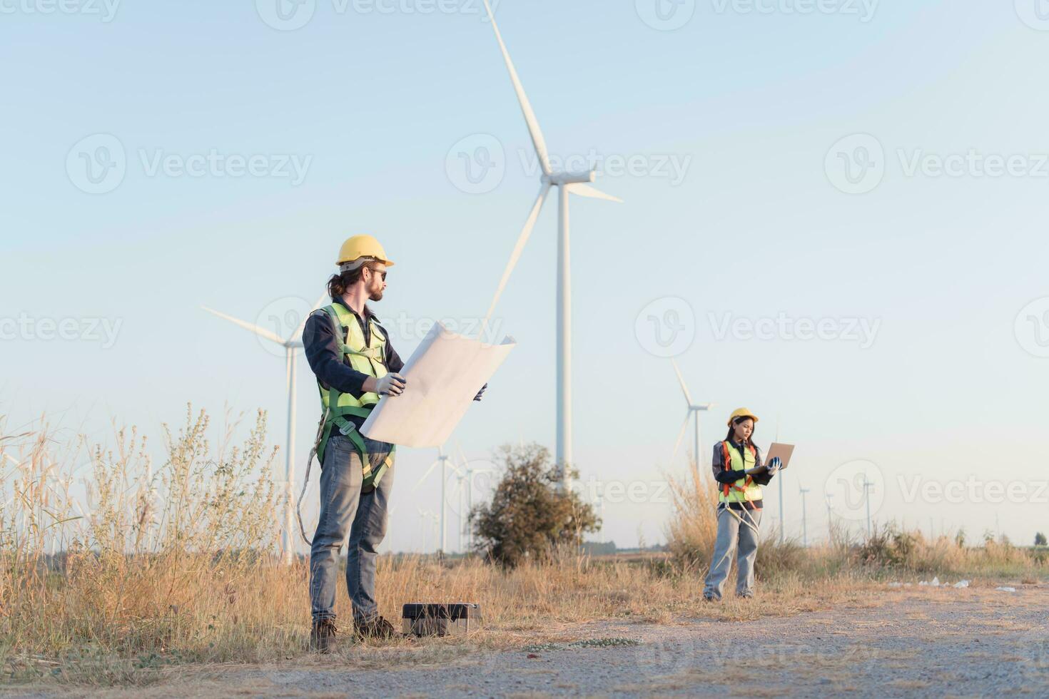 joven hombre ingeniero vistiendo la seguridad casco y participación Plano en viento turbina granja. foto