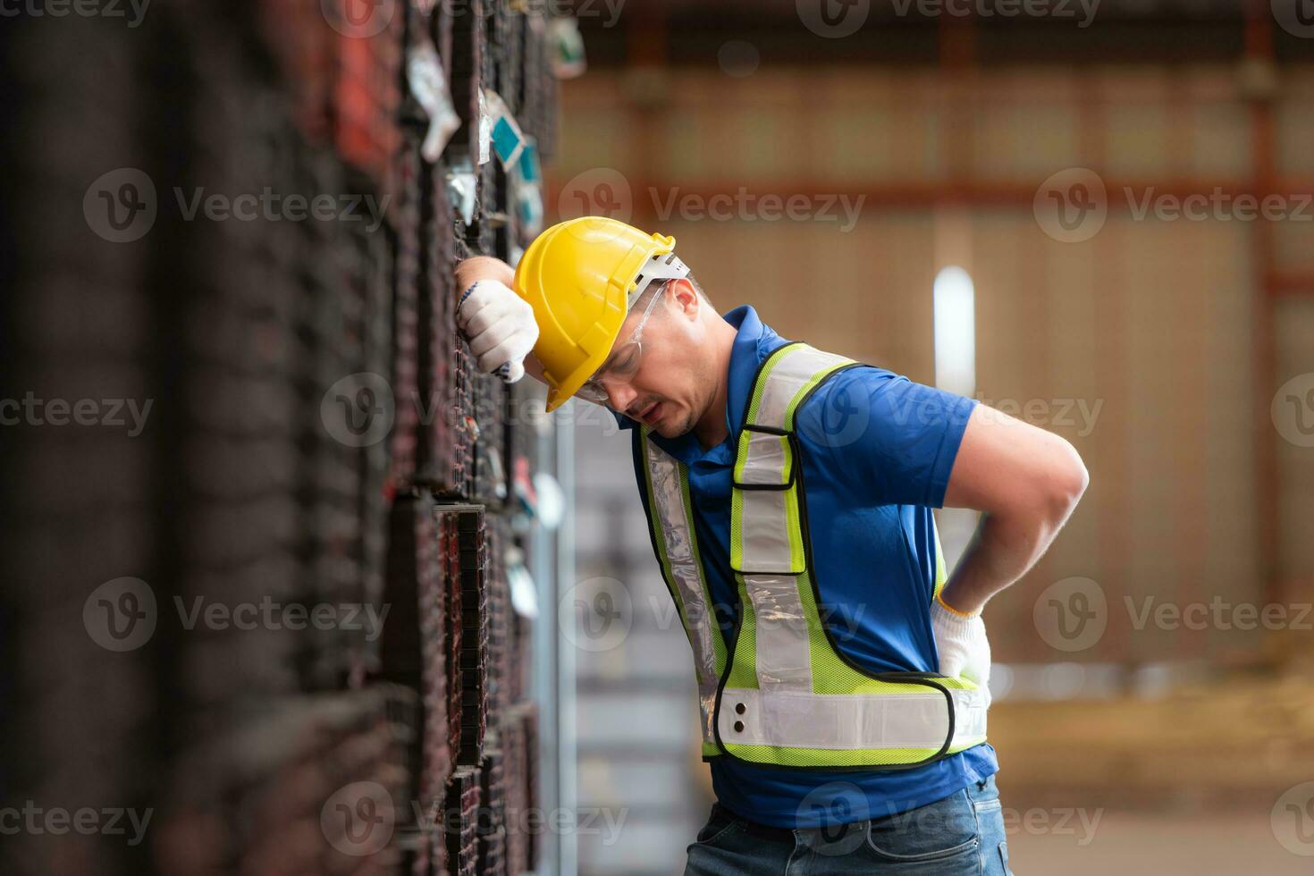 Portrait of a male worker wearing a safety vest and helmet standing on a steels pallet due to back pain from working in a factory lifting heavy things. photo