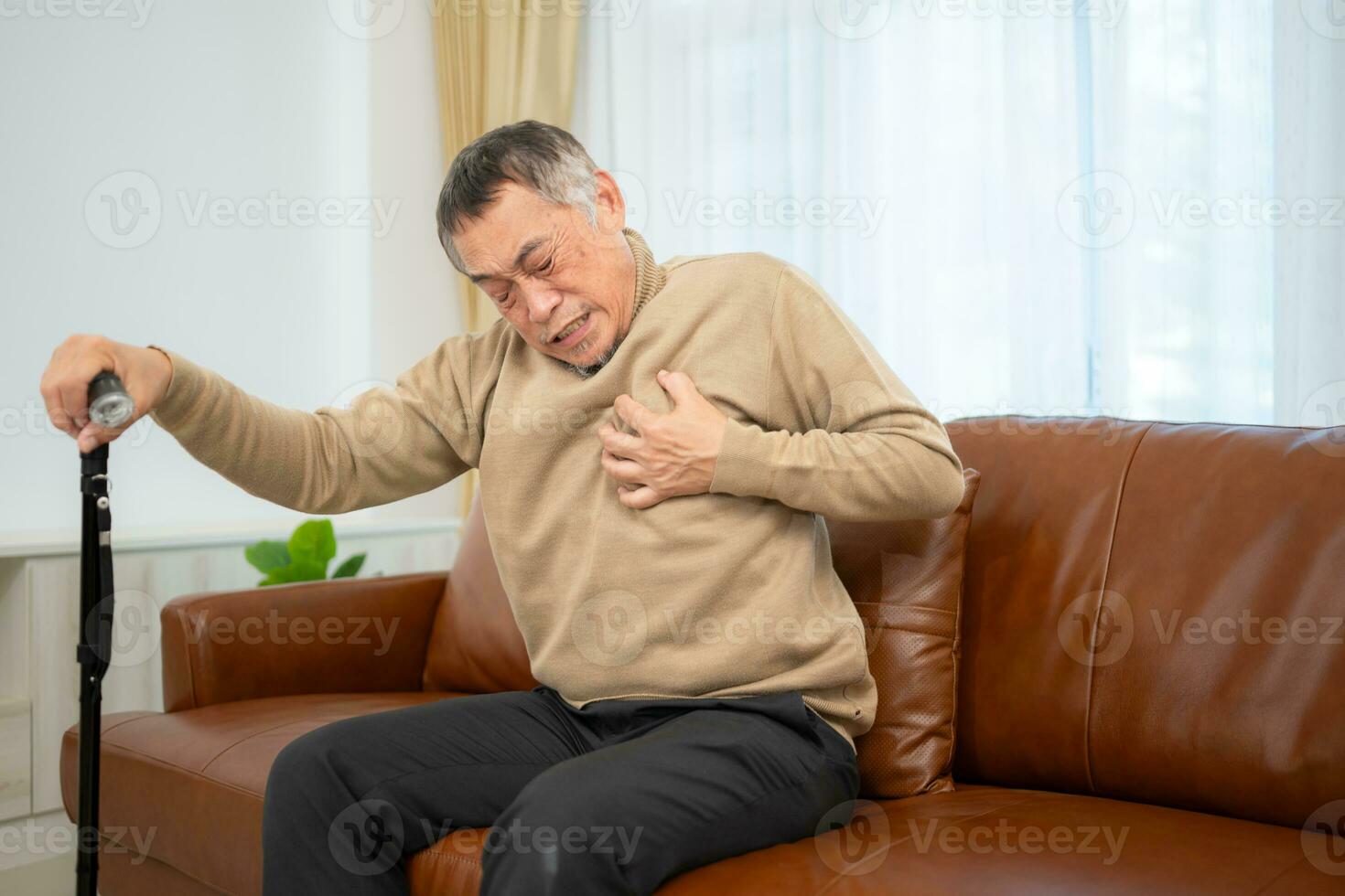 With heart disease symptoms, a senior guy sits on a sofa with a walking stick in his living room at home. photo
