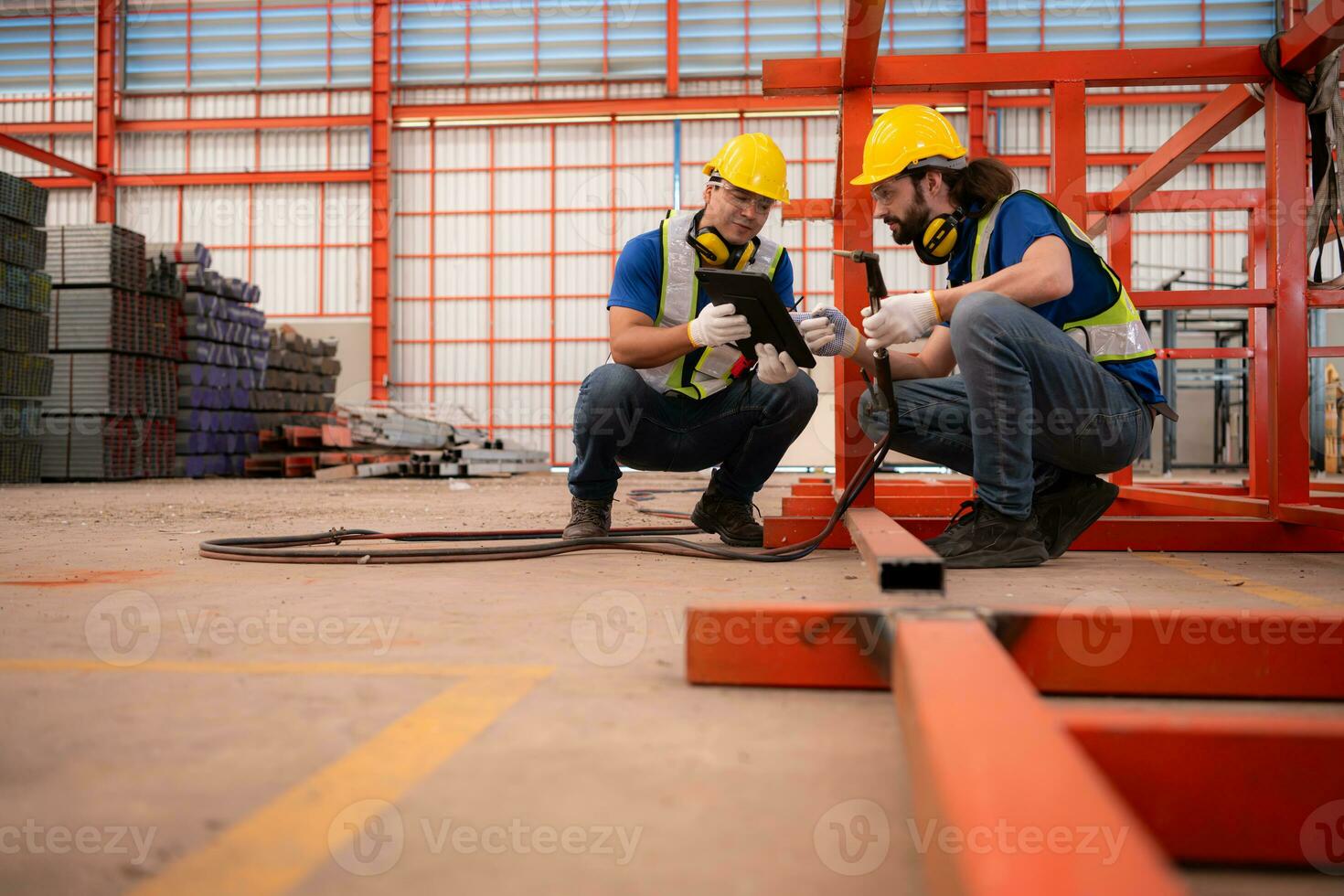 Portrait of two workers using digital tablet sit in front of the red steel structure photo