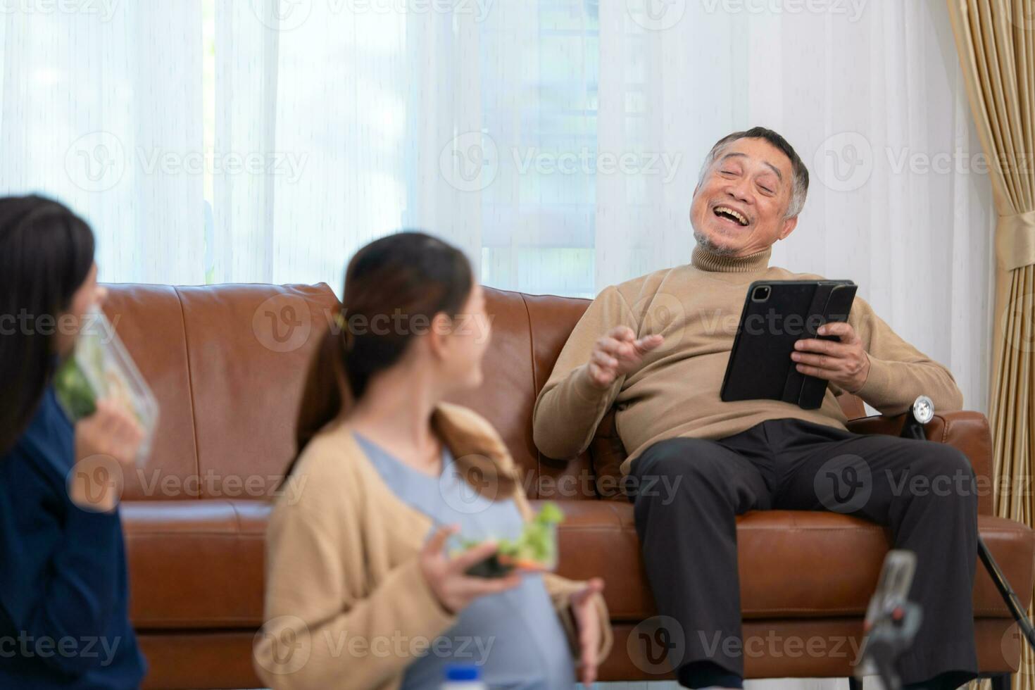 A pregnant asian woman sits on the floor with her younger sister. Live social media broadcast selling pregnant mothers' products and meals, There is a father in the background relaxing on a sofa. photo