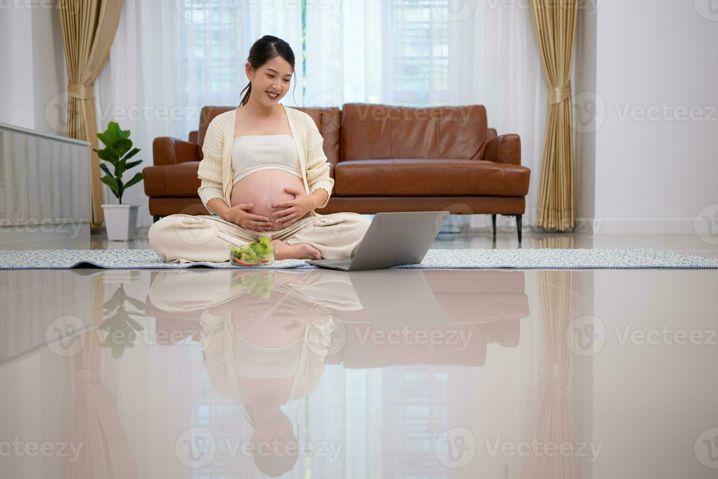 Pregnant woman eats salad as a snack while sitting on the floor of her home. photo