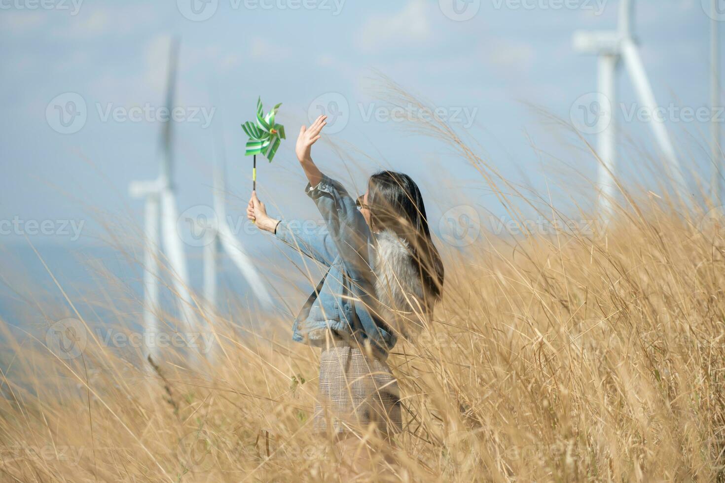 Young gorgeous brunette woman with long hair wearing a blue jacket, black sunglasses, and holding a miniature windmill photo