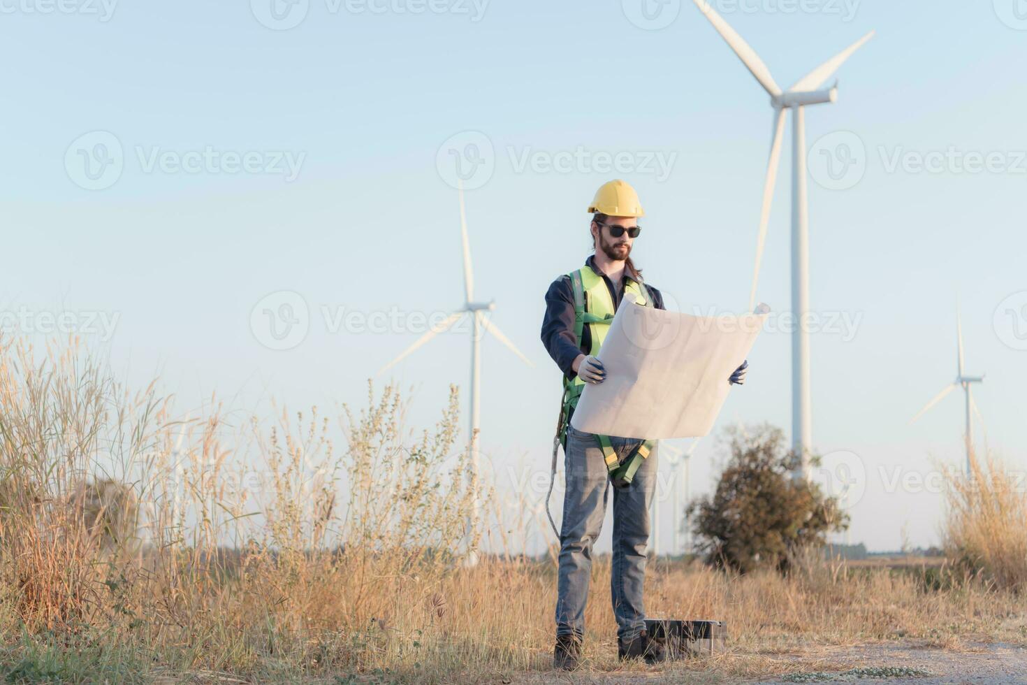 joven hombre ingeniero vistiendo la seguridad casco y participación Plano en viento turbina granja. foto