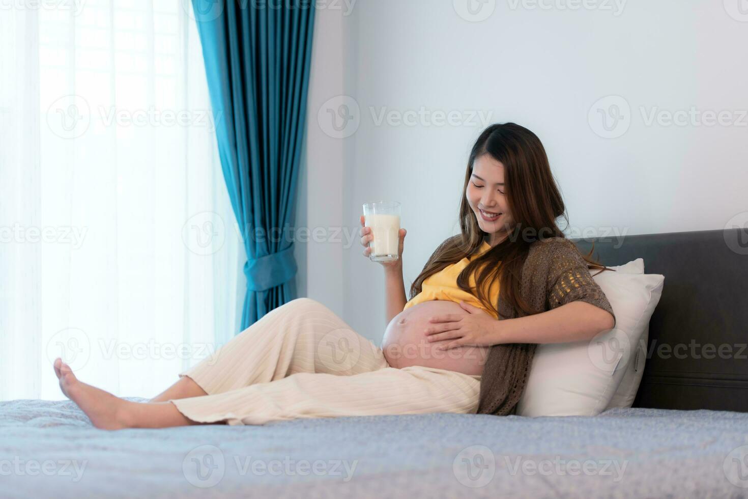 retrato de hermosa asiático embarazada mujer Bebiendo Leche en dormitorio a hogar foto
