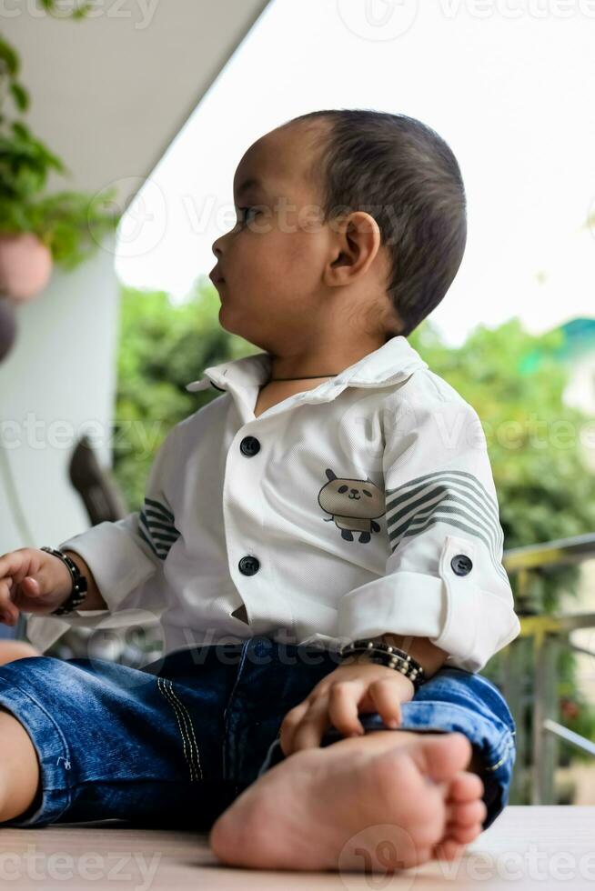 Baby boy at home balcony. Bright portrait of happy child sitting on the table. Little 1 year old boy during the day light at house balcony. photo