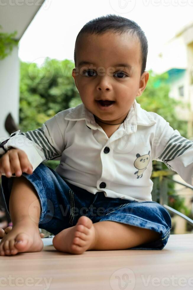 Baby boy at home balcony. Bright portrait of happy child sitting on the table. Little 1 year old boy during the day light at house balcony. photo