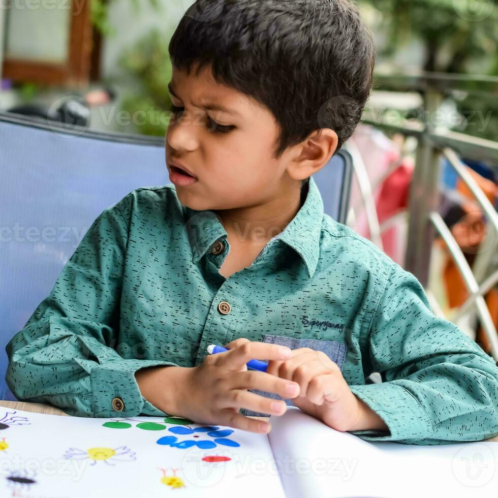 Smart Indian little boy perform thumb painting with different colourful water colour kit during the summer vacations, Cute Indian Kid doing colourful thumb painting drawing on wooden table photo