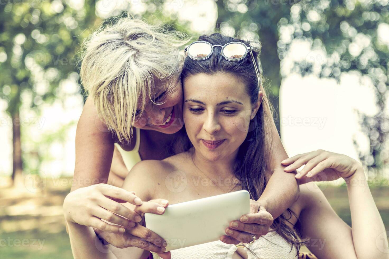 madre y hija en traje de baño teniendo divertido acecho un digital tableta foto
