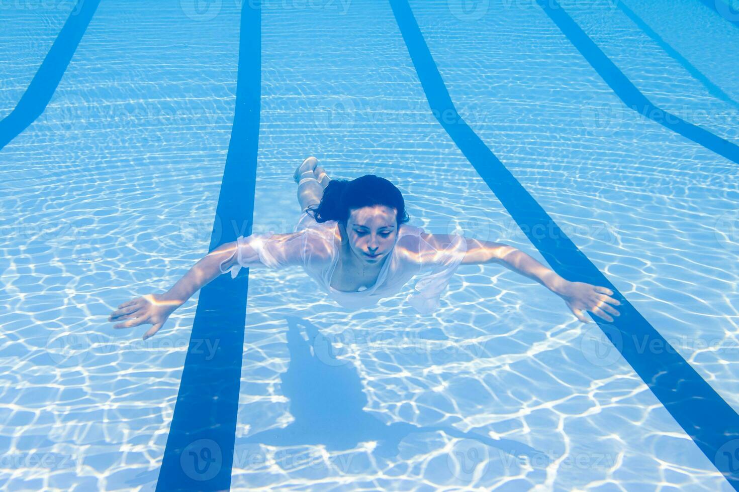 joven niña en traje de baño flotante en azur agua de nadando piscina en luz de sol foto