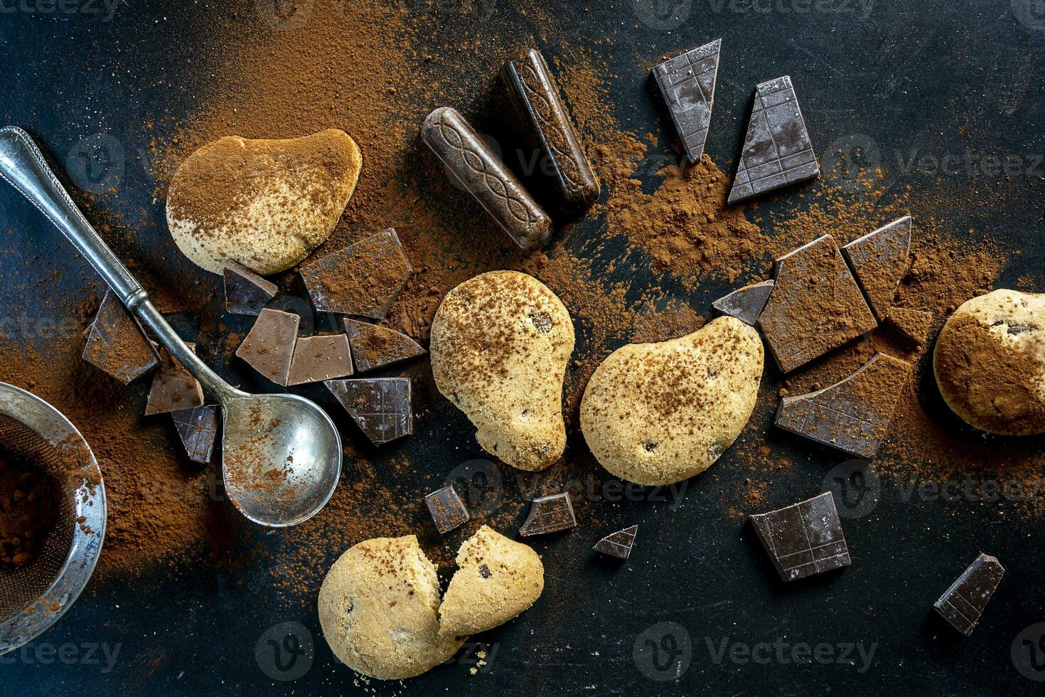 cookies and pieces of chocolate sprinkled with cocoa powder on a black background photo