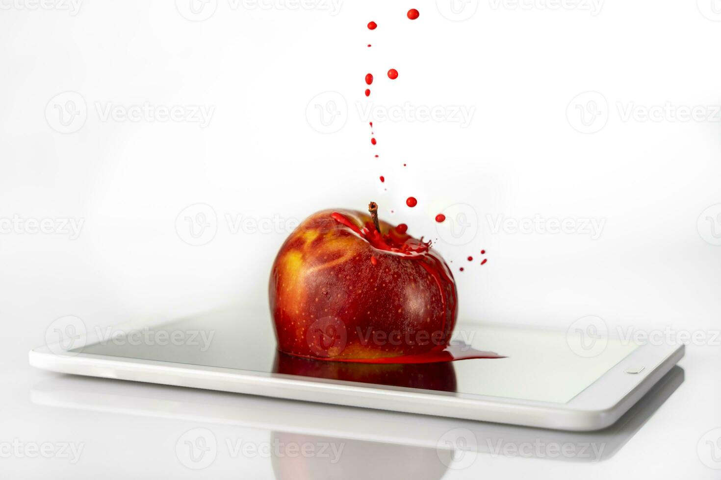red apple is sinking into the viewer of a tablet on white background photo