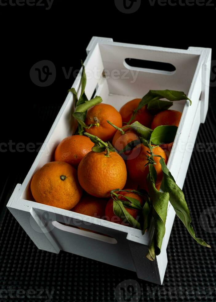 wooden box full of tangerines with green leaves photo