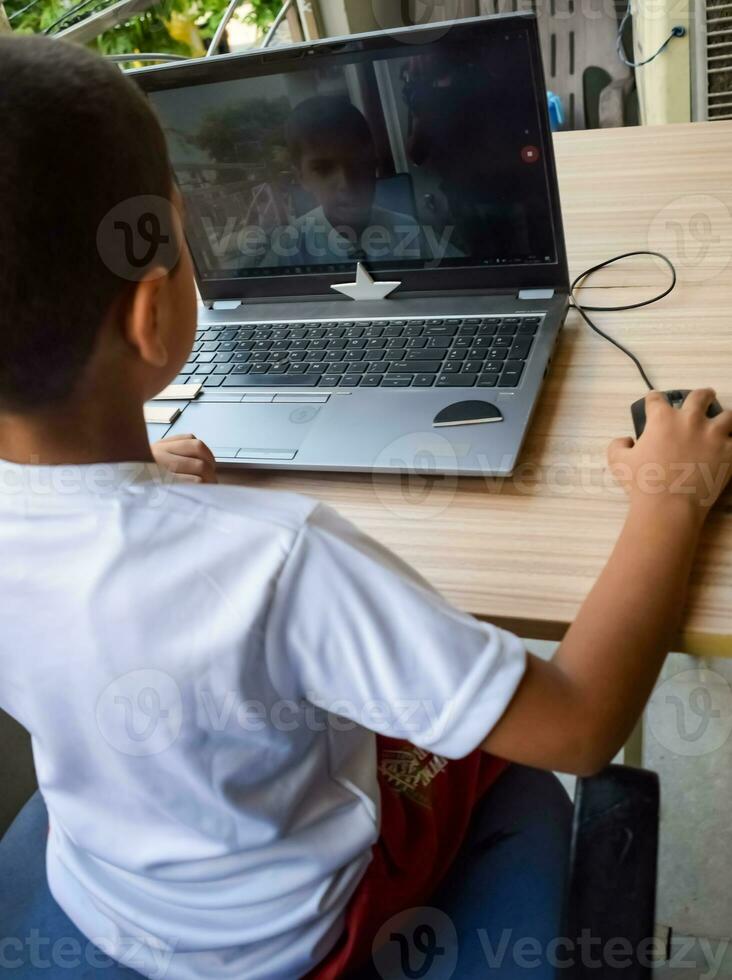 Little boy sitting at table using laptop for online class in Grade 1, Child studying on laptop from home for distance learning online education, School boy children lifestyle concept photo