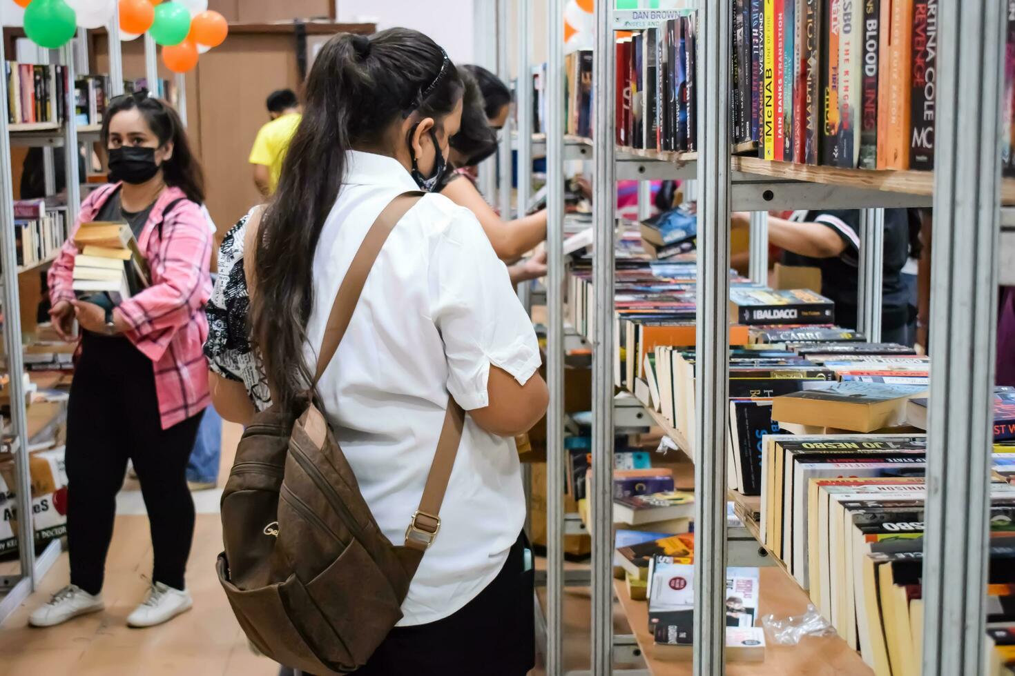 Delhi, India, September 09 2023 - Various age group people reading variety of Books on shelf inside a book-stall at Delhi International Book Fair, Selection of books on display in Annual Book Fair photo