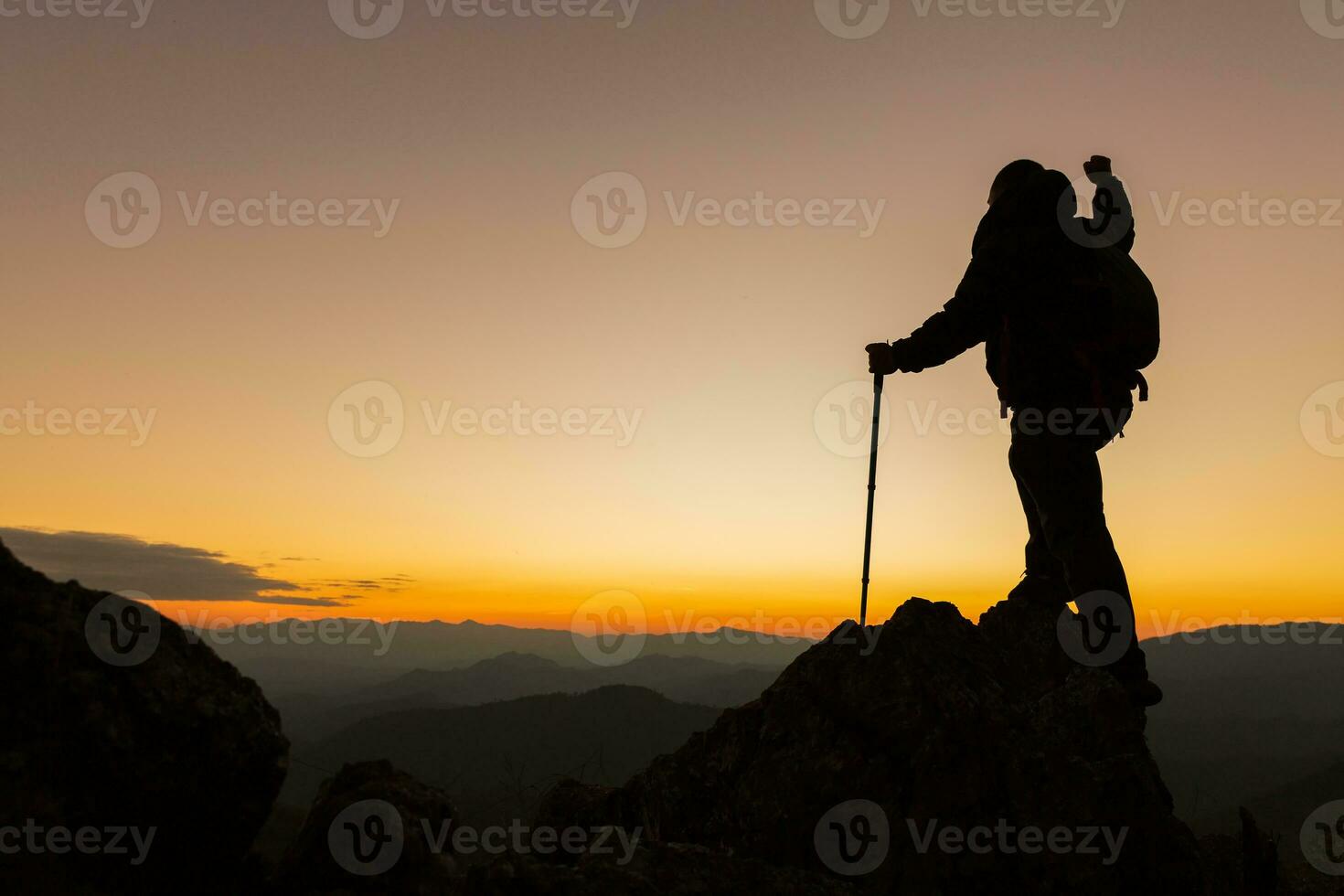Silhouette of a hiker man on a rock pedestal with hands up. Beautiful orange sunset. Independent hiking travel, success. photo