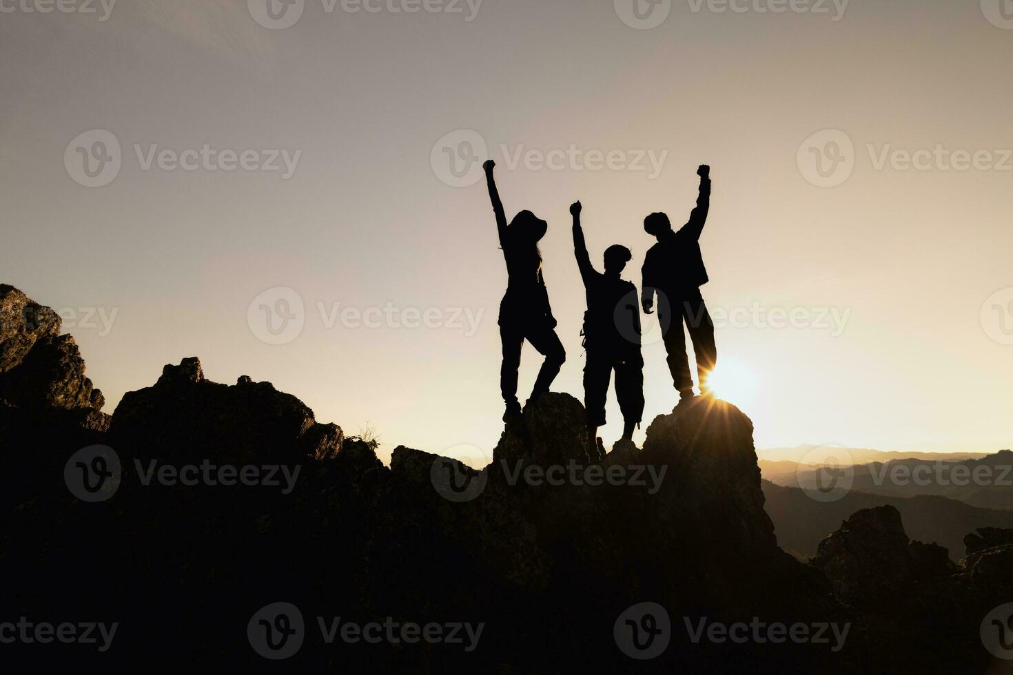 Happy friends hikers or tourists stands with raised arms on mountain top against mountains and looking at sunset. Independent hiking travel, success. photo