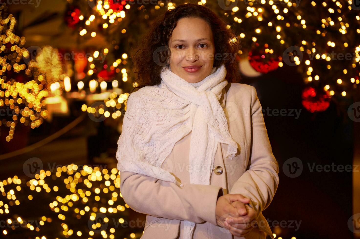 hermosa mujer en calentar ropa, sonriente mirando a cámara, en pie en contra iluminado calle antecedentes foto