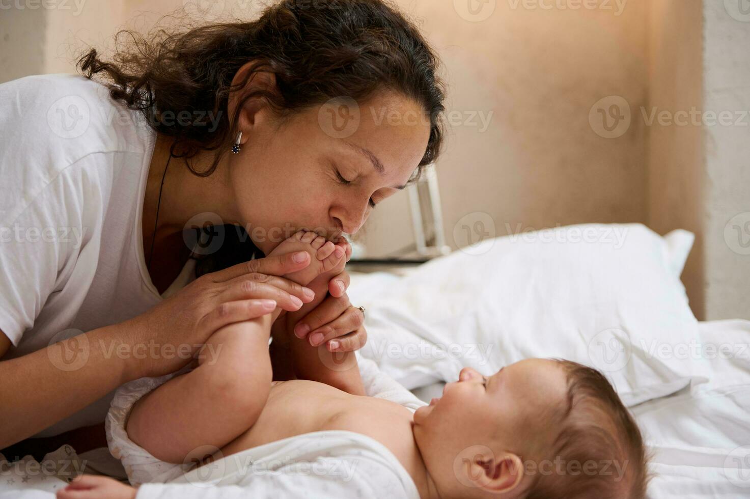 Closeup young loving caring mom gently kisses little feet and tiny toes of her newborn baby boy, enjoying spending tender moments with her beloved kid. Mother and child connection. Baby care concept photo