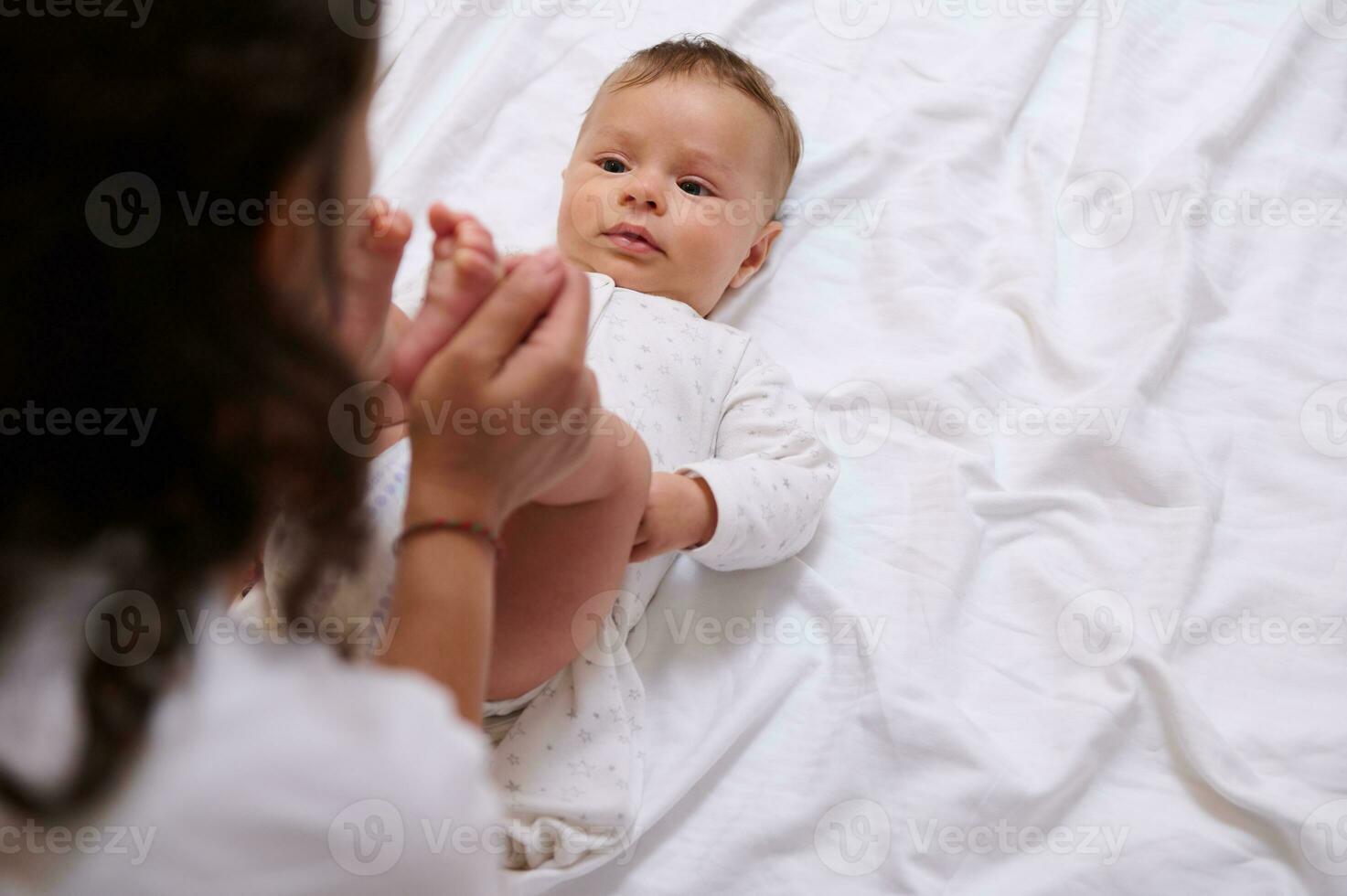 Overhead view of a loving mom kissing little feet and tiny toes of her adorable beloved baby boy. Copy advertising space photo